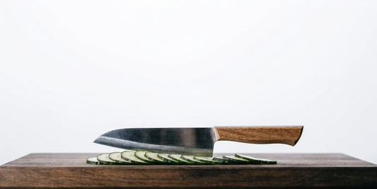 Santoku-Messer neben hauchdünn geschnittenen Gurkenscheiben auf dunklem Holz