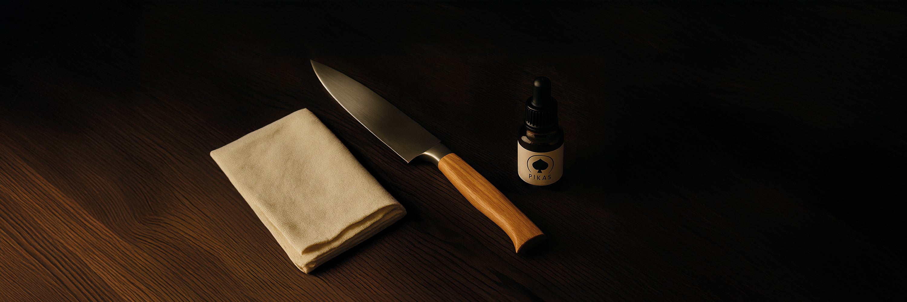 Professionelles Messerpflege-Set mit PIKAS Pflegeöl, großem Baumwolltuch und scharfem Küchenmesser auf dunkler Holzoberfläche